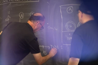 Two men are standing at a whiteboard, performing calculations on TPU tubes